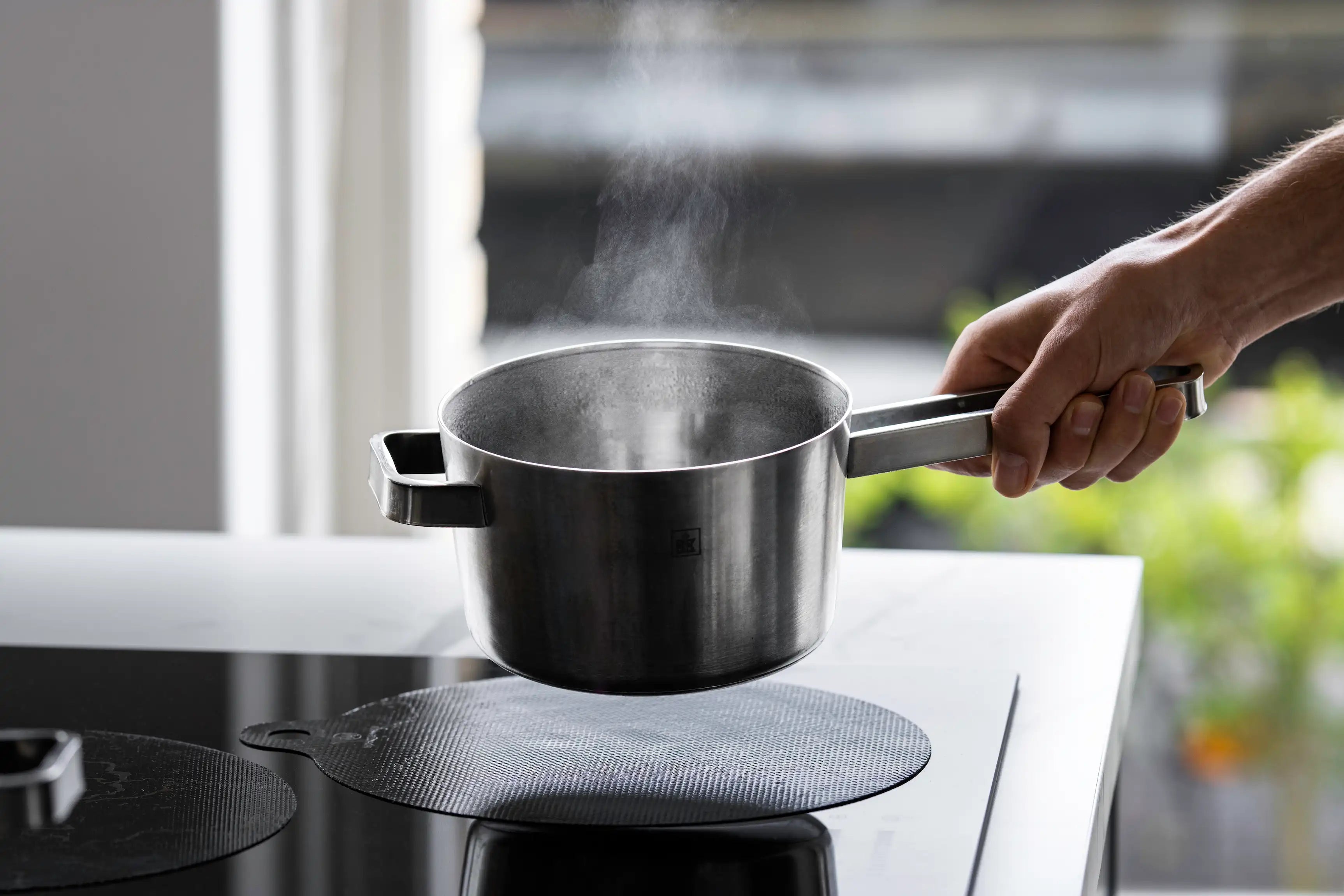 Kookpan wordt opgetild boven een inductiebeschermer op een inductiekookplaat.