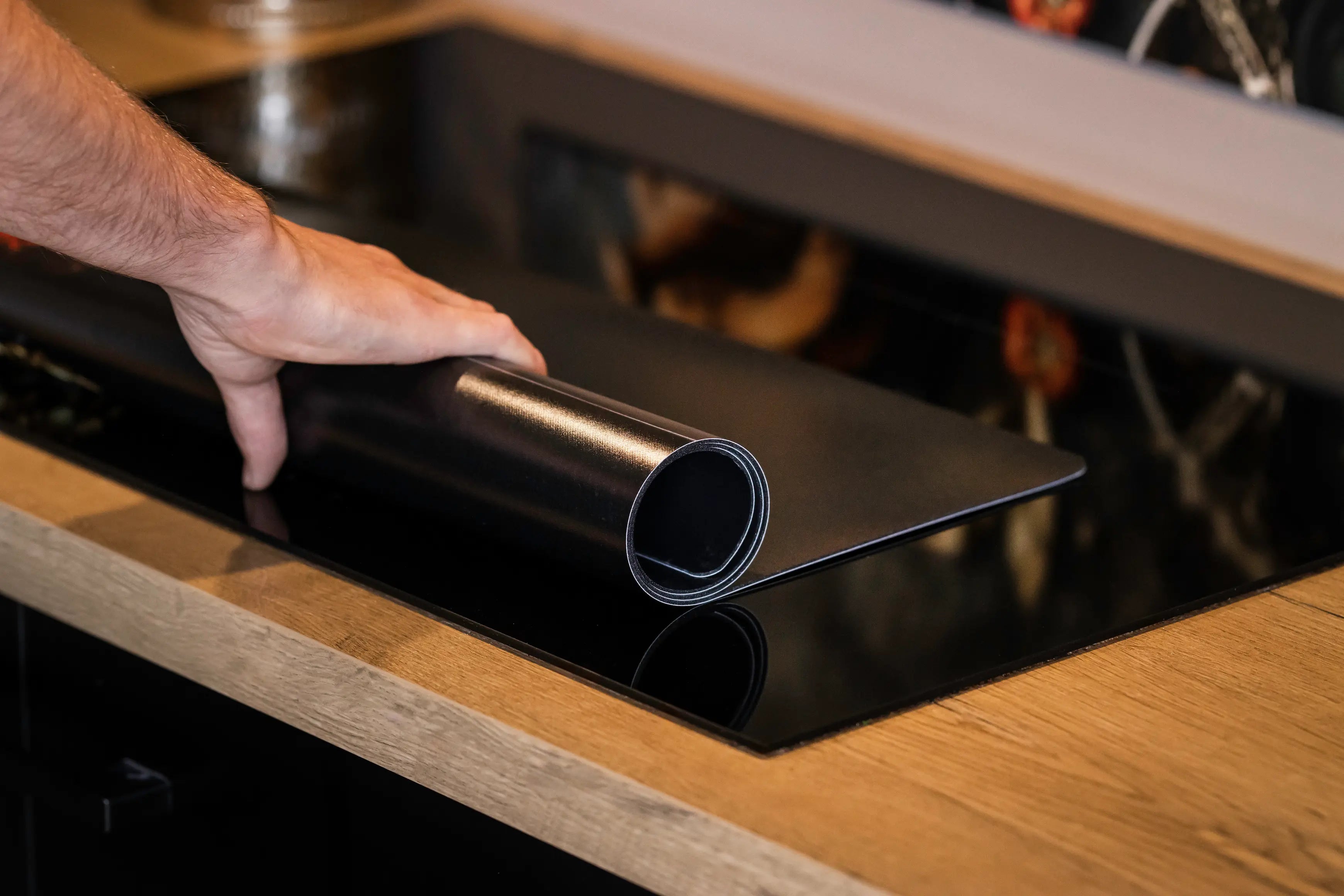 Inductiebeschermer die opgerold wordt op een inductiekookplaat in de keuken